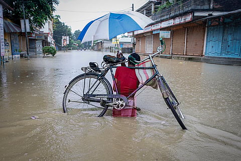 Flood in Tripura: A man carrying a bicycle on his back wades through a flooded road